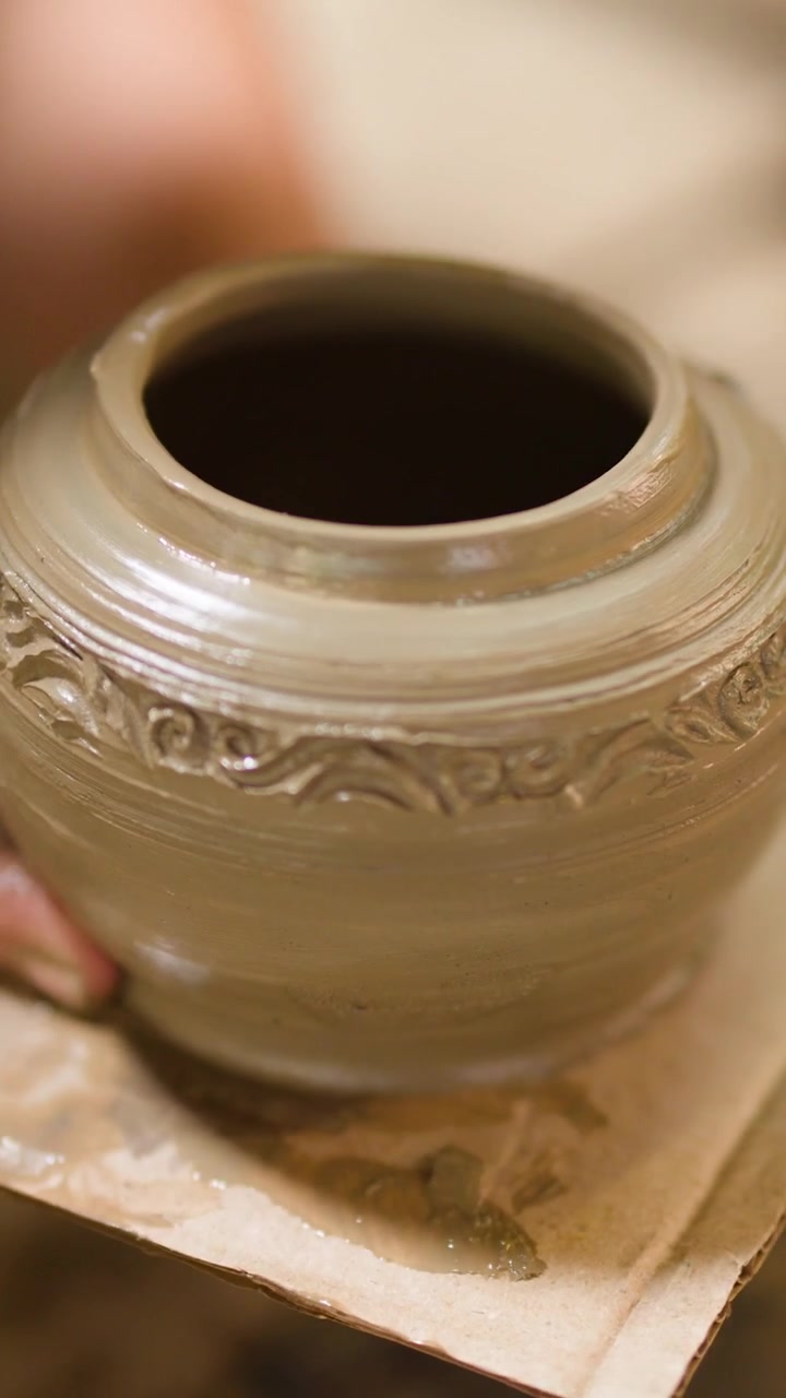 Primo piano delle mani di un vasaio che sollevano con cura un recipiente di argilla bagnato da un tornio