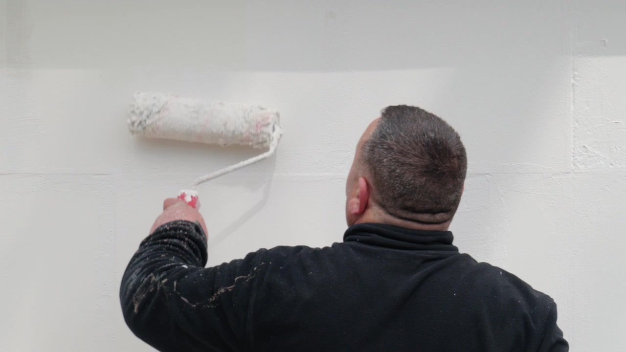 Worker painting a wall with a roller, renovation process in progress