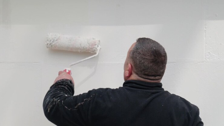 Worker painting a wall with a roller, renovation process in progress