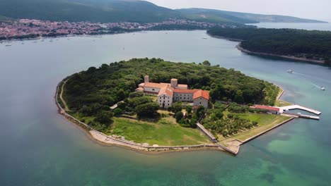 aerial rotating view of kosljun island in punat bay on krk island in croatia with a small monastery on it