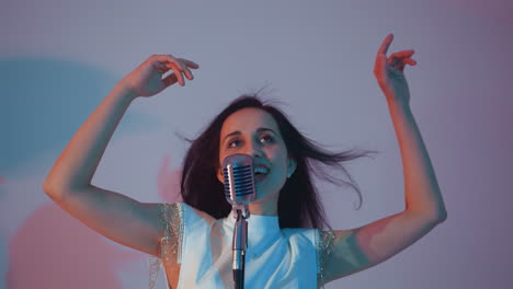 singer in a white gown smiling with hands up in the air, performing joyfully into a vintage microphone. her hair is flowing against a soft gradient background of pink and blue