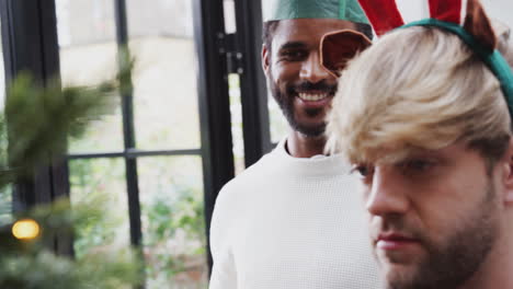 pareja de hombres homosexuales en casa colgando decoraciones en el árbol de navidad juntos