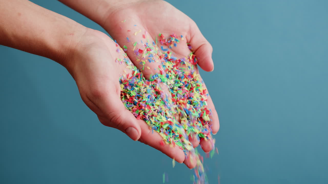Hands holding and pouring colorful shredded plastic