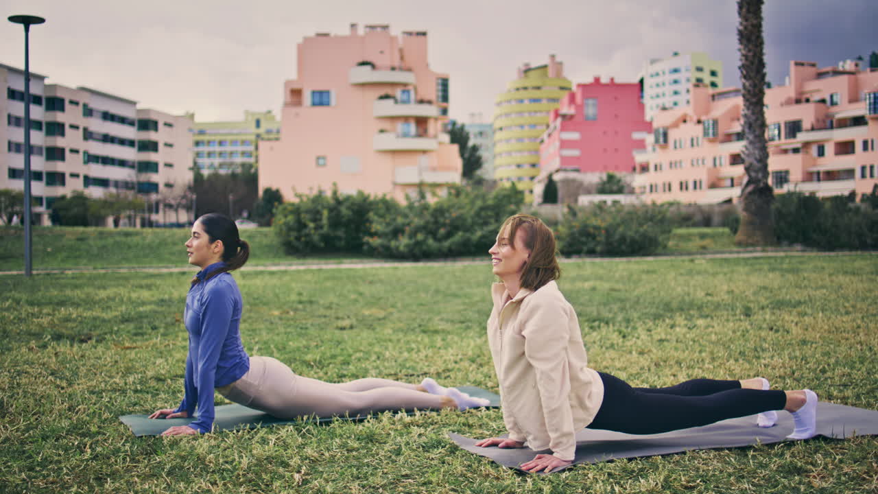 Yogini bending exercises in city park. Relaxed sports women practicing yoga
