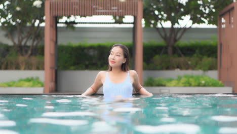 Water-level-shot-of-a-pretty-young-Asian-woman-lounging-along-the-back-wall-of-an-infinity-pool
