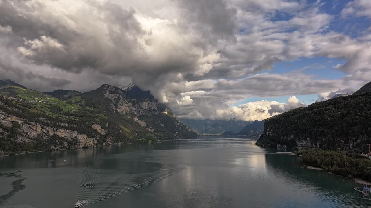 Hyperlapse drone footage over Lake Walensee, showcasing a beautiful scene with abundant clouds and snow-capped mountains in the background.