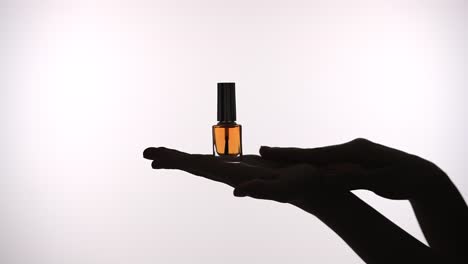 elegant display of nail polish bottle against deep in silhouette a hand gracefully holds a bottle of nail polish silhouetted against a deep orange background emphasizing elegance