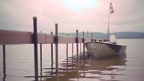 Kleines-Boot,-Das-Während-Des-Sonnenuntergangs-In-Einem-Ruhigen-See-Mit-Wunderschönem-Landschaftshintergrund-An-Holzdock-Gebunden-Ist-4k-Prores