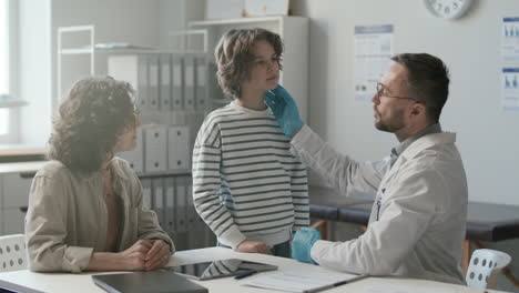 médico examinando los ganglios linfáticos del niño y hablando con su madre en la clínica