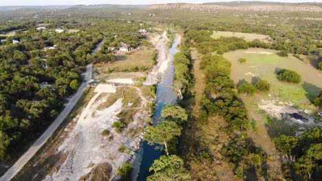 Flying-down-the-river-at-sunset-over-large-cypress-trees-and-hill-country-in-the-distance---Aerial-footage-of-the-Blanco-river-in-Wimberly,-TX