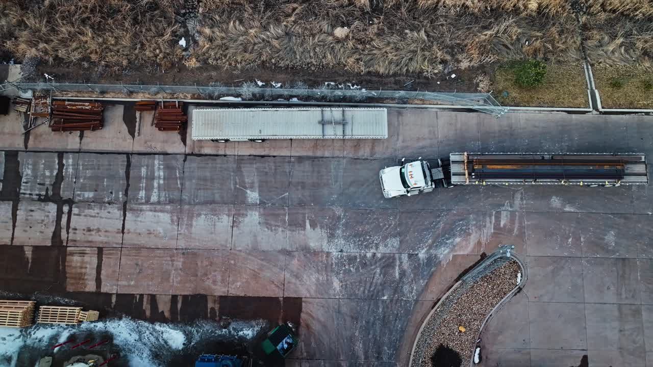 Drone top down descend on semi truck and trailer loaded with steel beams driving to leave factory