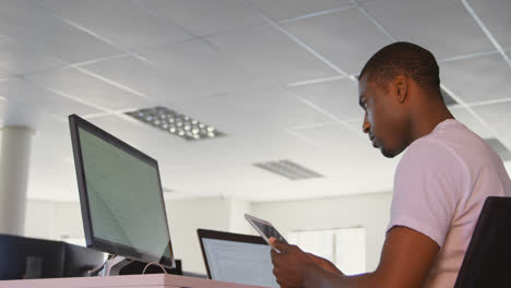 Vista-Lateral-De-Un-Joven-Ejecutivo-Negro-Trabajando-En-Una-Tableta-Digital-En-El-Escritorio-De-Una-Oficina-Moderna-4k