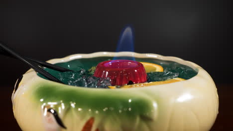 tropical tiki style cocktail in large bowl with orange slices, burning flame sake punch beverage, slider close up 4k