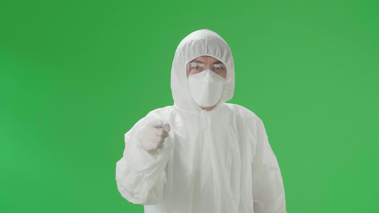 Angry Asian Man Wearing Personal Protective Equipment Uniform Ppe, Medical Face Mask And Pointing Displeased And Frustrated To The Camera In The Green Screen Studio
