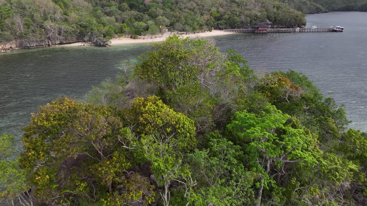 Aerial over rock formation to small beach with pier. Gua Rangko, Labuan Bajo, Indonesia.