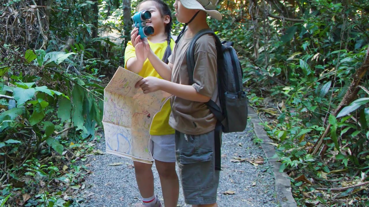 Young boy and girl explore a forest trail using a map and binoculars during daytime.