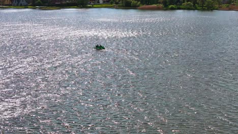 epansive, high-angle wide-shot captures a lone dark boat on the shimmering, sun-dappled surface of biržai's lake during a bright, sunny summer day, with distant green shores