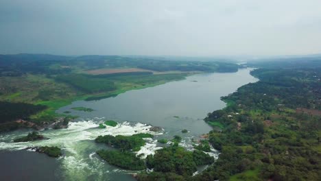 aerial view of the nile river flowing through lush green ugandan landscape, showcasing the source of the world's longest river in jinja, with whitewater rapids and forested islands, drone pulling out