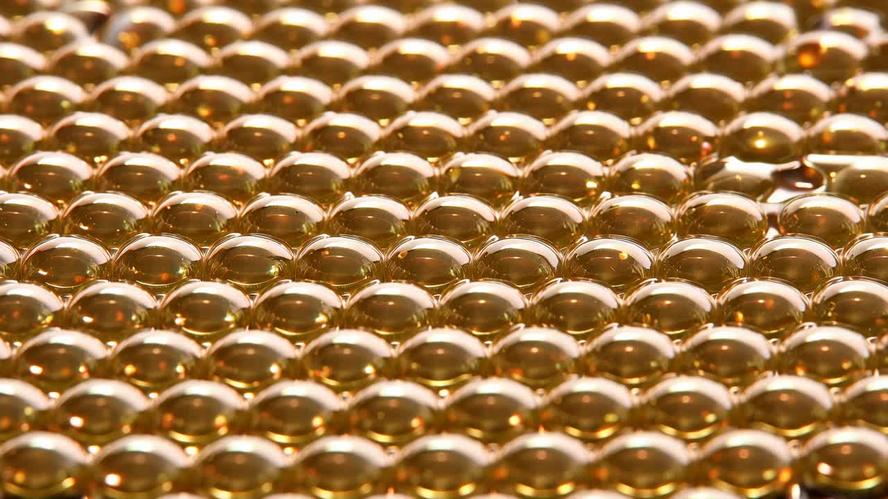 Mostra la camera macro che si sposta su una serie di goccioline ambrate su un tavolo, evidenziando le inclusioni più scure