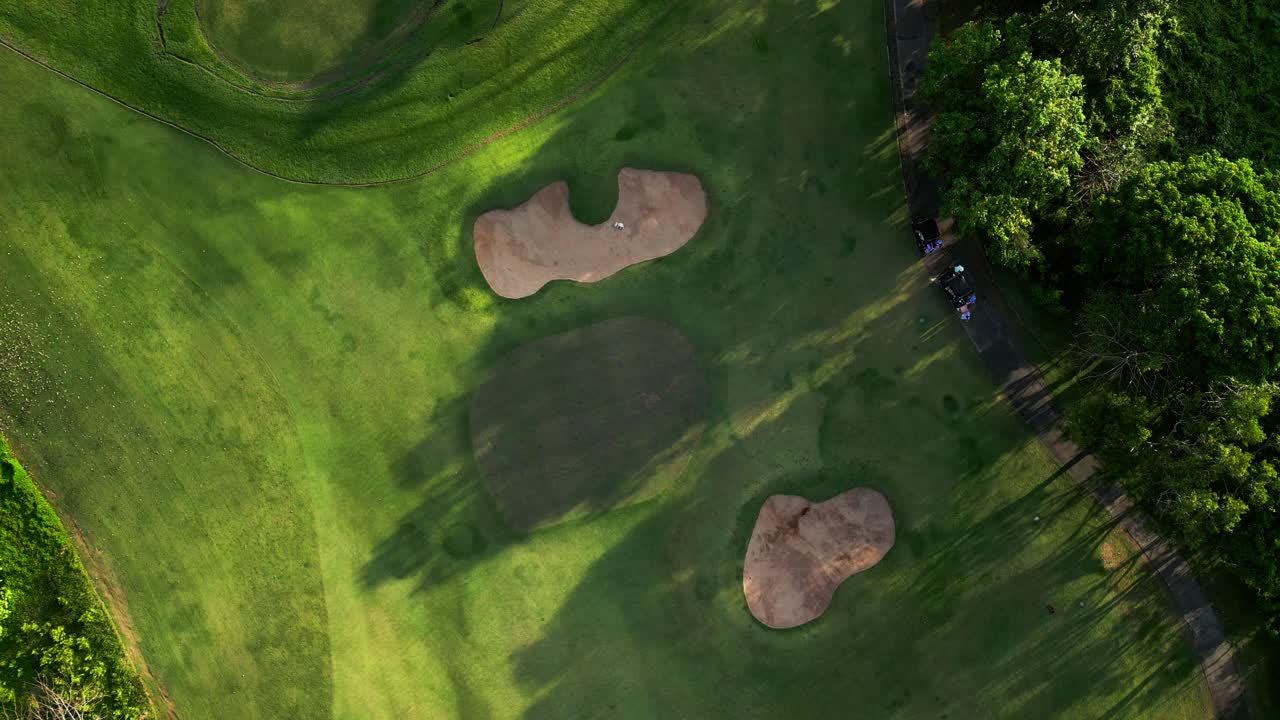 Overhead drone view of a tropical Bali golf course surrounded by lush greenery and palm trees, capturing players on the fairway and the serene landscape of this scenic island resort destination