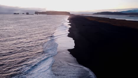 a tranquil black sand beach at reynisfjara, iceland, stretches into the distance, reflecting the soft hues of a sunset or sunrise over the calm north atlantic waters