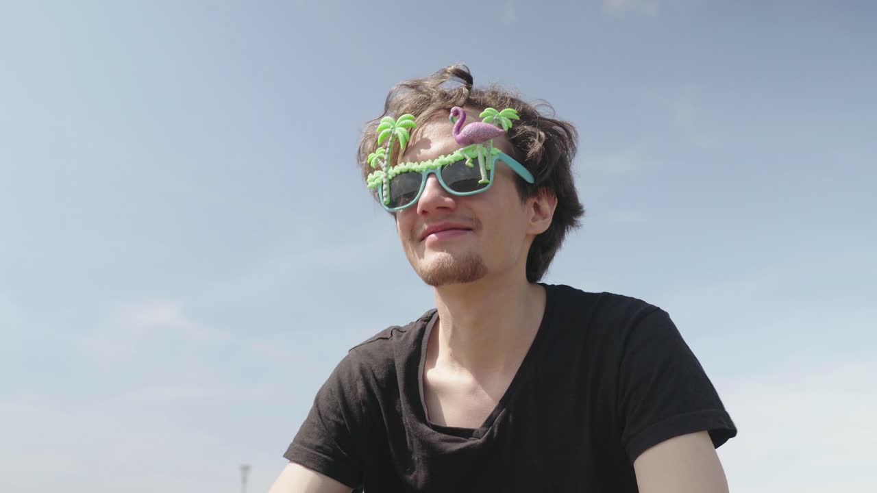 젊은 남자는 미친 다채로운 안경을 입고 음악적 비트에 움직입니다.