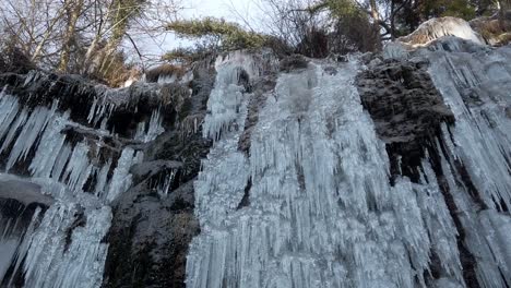 Trozos-De-Hielo-Colgados-En-La-Pared-De-Piedra-Con-Gotas-De-Agua,-Jungla-Y-Cielo-En-La-Parte-Superior