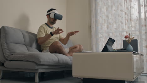 man simulates playing piano or dj set in air using vr headset while seated on couch at home