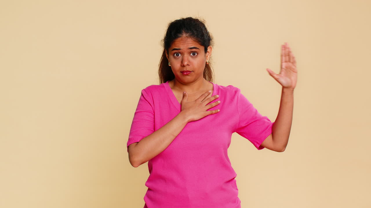 Indian woman raising hand and placing other on heart solemnly performing oath or pledge gesture