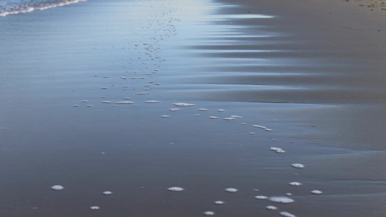 Washing surf pushing wet shoreline shifting foam patches and showing ripple bands with pebble trail