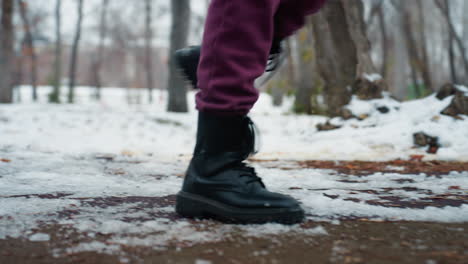 side leg view of person wearing black boots jogging on snowy ground in outdoor park, urban setting, cold weather, fitness in winter, exercising in chilly environment, winter workout