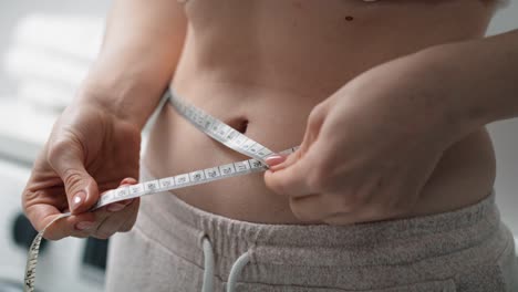 close up of caucasian woman standing in the bathroom and taking measures on her waist.