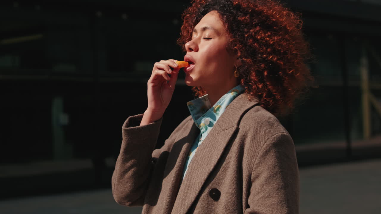 Young Woman Eats Orange Slice in City