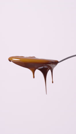 vertical video of melted chocolate dripping from overflowing spoon against white background with copy space