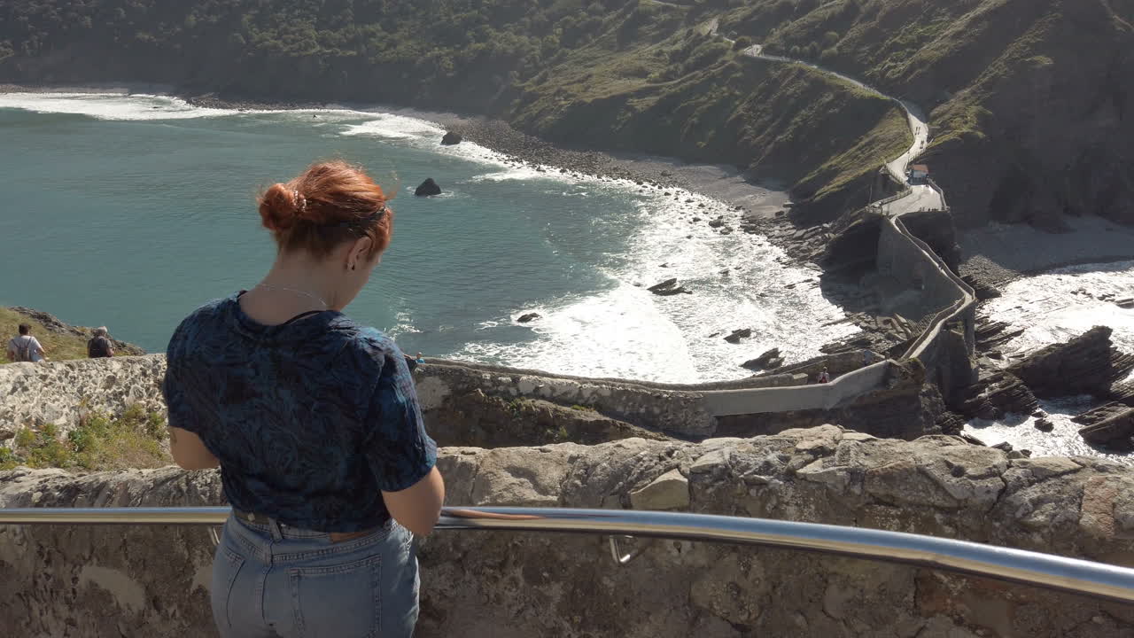 Woman taking a picture of San Juan de Gaztelugatxe