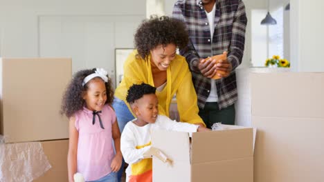 vista frontal de una familia negra desempaquetando cajas de cartón en un hogar cómodo 4k