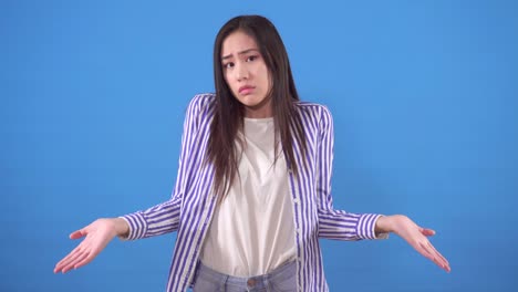 confused and indignant young woman in a shirt stands on the blue background