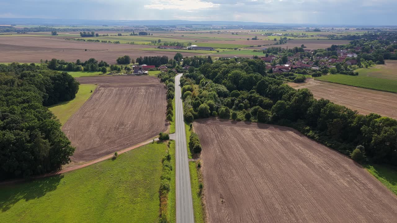 Road leading to a picturesque village amidst fields and meadows. Natural landscape with tranquility. Drone view
