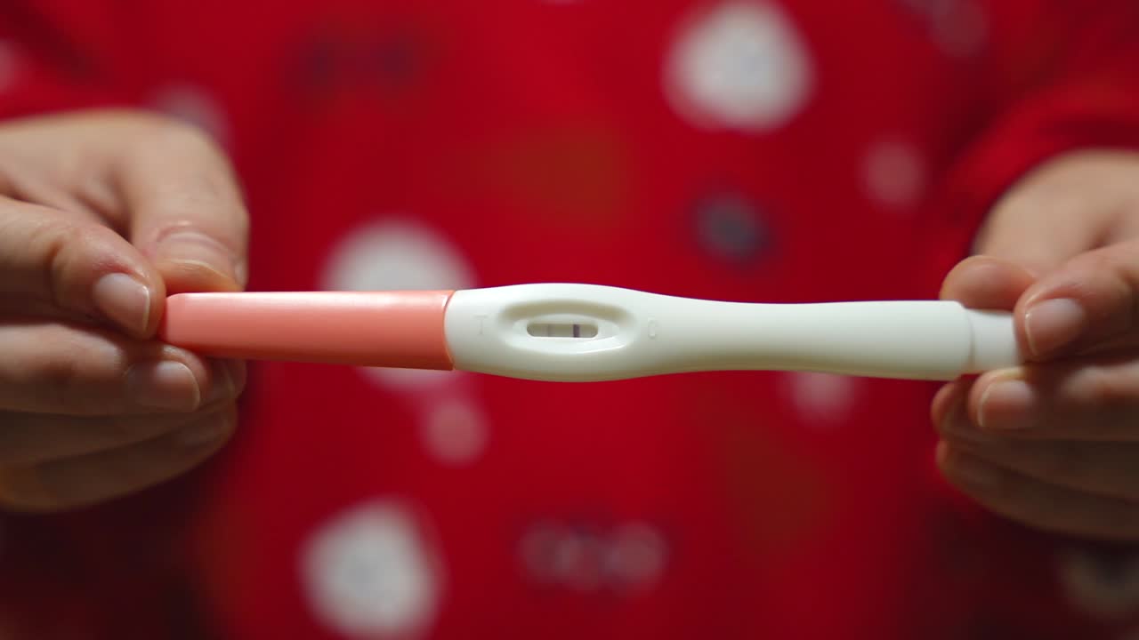 Positive pregnancy test held by the hand of a pregnant woman wearing red Christmas pajamas