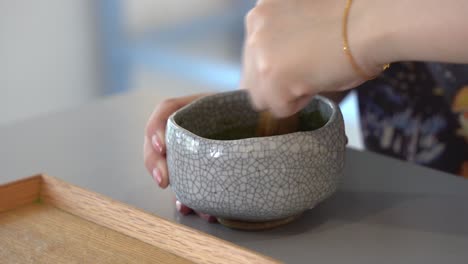 female hands mixing match green tea in the ceramic bowl with bamboo whisk, close up handheld shot capturing preparation of traditional japanese beverages, specialty drinks