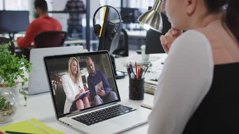 Caucasian-woman-having-a-video-call-with-male-and-female-office-colleague-on-laptop-at-office