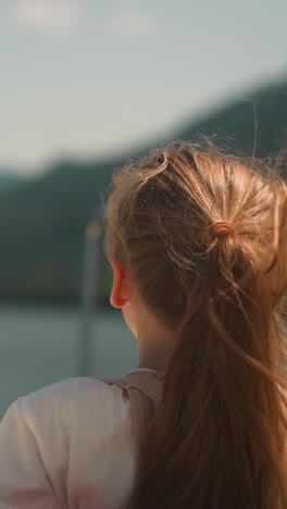 little girl wearing scoliosis brace enjoys tourist boat rocking on ocean bay waves backside view. child with back disease travels by yacht across sea