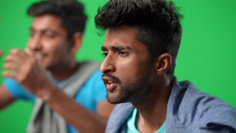 side view portrait of emotional anxious middle eastern man cheering with friend supporting football team on green screen. worried young fans yelling gesturing at chromakey background.