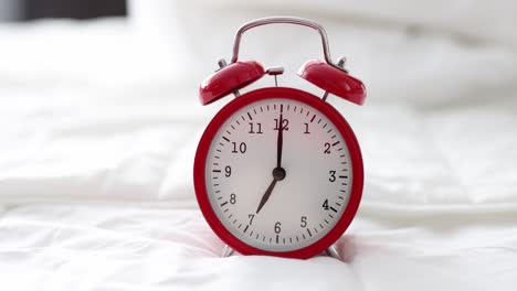 red alarm clock for seven in morning is on bed