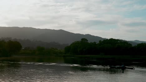 Evening-sky-over-a-quiet-creek-as-a-kayaker-paddles-by-with-foothill-and-trees-in-the-background