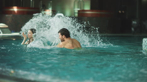 Smiling-couple-splashing-in-pool-at-hotel.-Cheerful-couple-having-fun-in-water