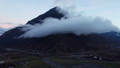 Aerial-pedestal-up-offering-a-view-over-white-clouds-in-front-of-a-mountain-range-with-snowy-peaks