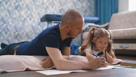 careful-father-helps-little-daughter-do-home-task-on-floor