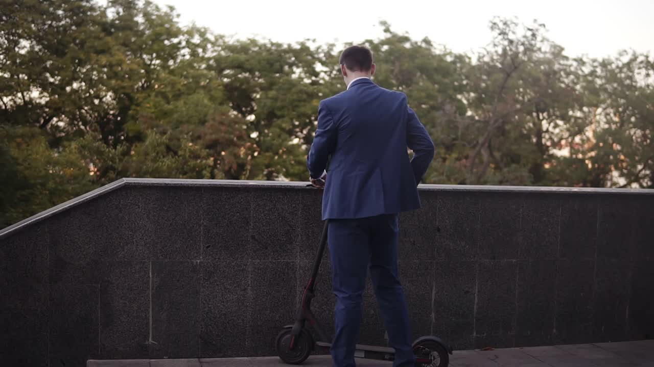 전기 스쿠터를 타고 전화 통화에 응답하기 위해 멈춘 사업가. 거리에서 스쿠터를 타고 웃는 사업가