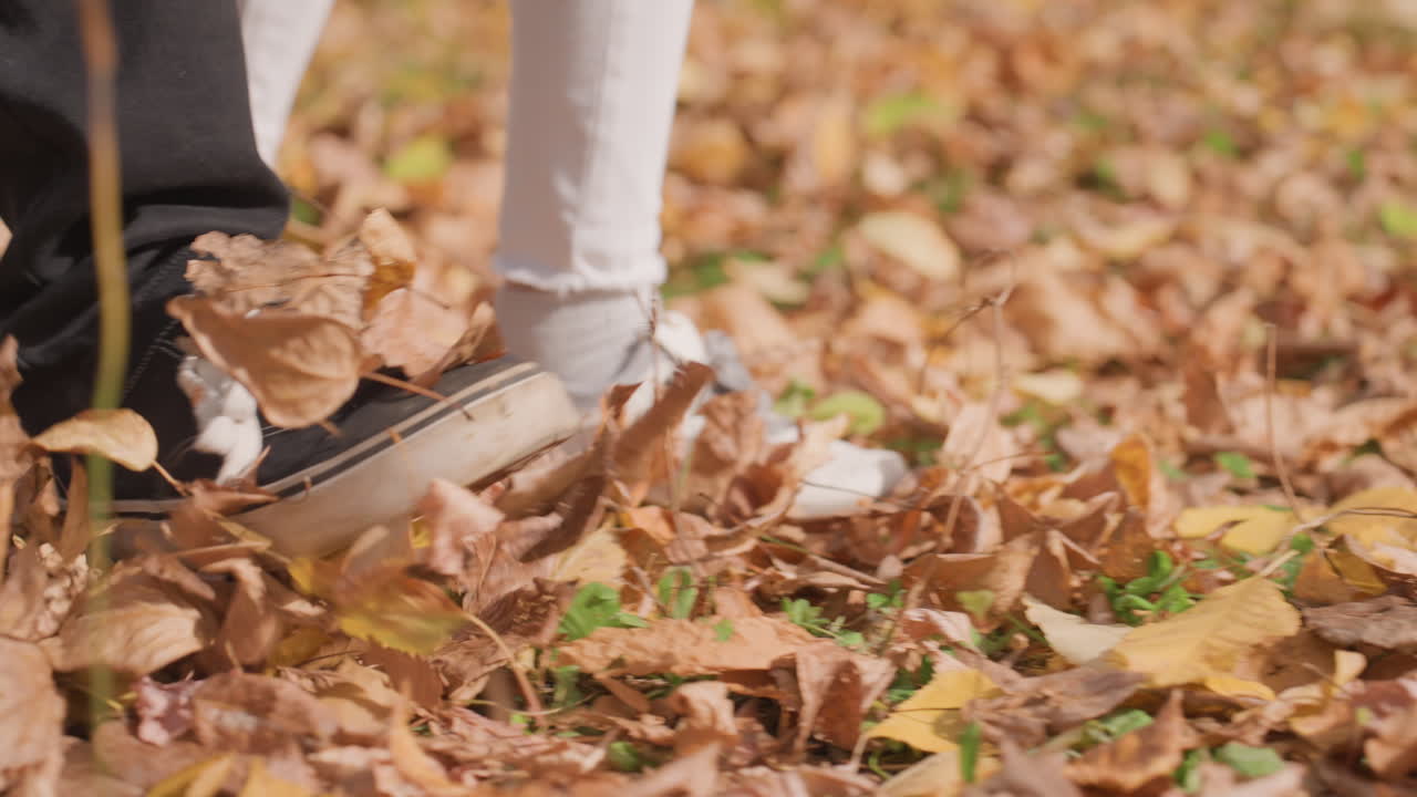Autumn leaves closeup of feet white married couple playfully stepping through crunchy golden foliage, sneakers and socks scuffing ground, intimate candid detail conveying romance, tenderness
